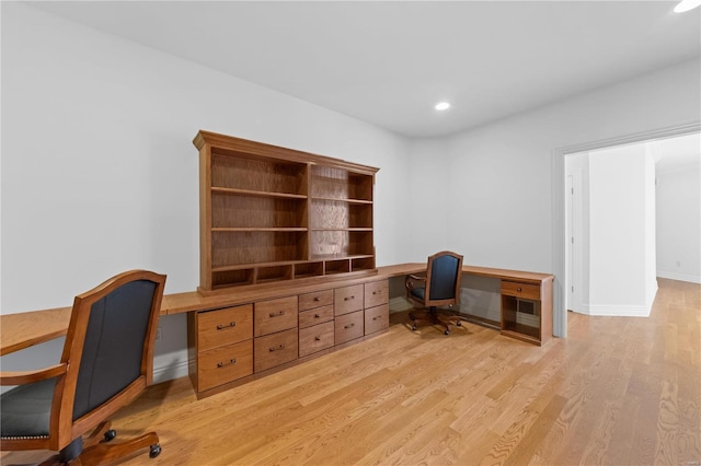 home office with built in desk and light hardwood / wood-style floors