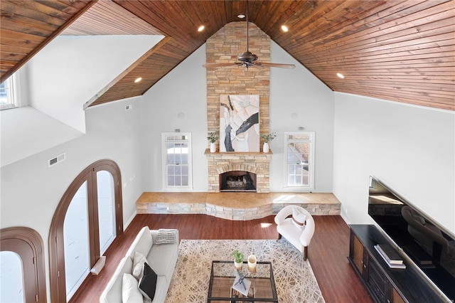 living room with ceiling fan, dark wood-type flooring, a stone fireplace, high vaulted ceiling, and wood ceiling