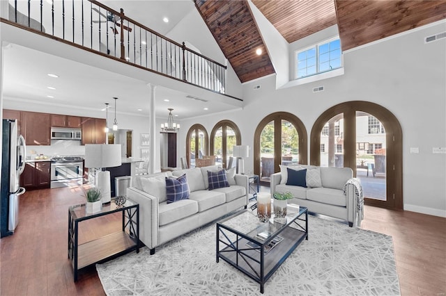 living room featuring a towering ceiling, wood ceiling, crown molding, hardwood / wood-style flooring, and an inviting chandelier