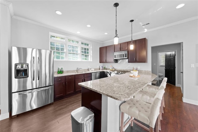 kitchen featuring hanging light fixtures, dark hardwood / wood-style floors, ornamental molding, appliances with stainless steel finishes, and a breakfast bar area