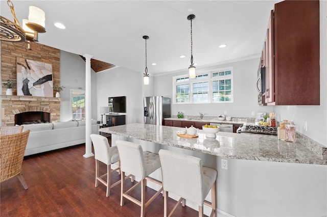 kitchen featuring hanging light fixtures, stainless steel appliances, light stone counters, kitchen peninsula, and a kitchen bar