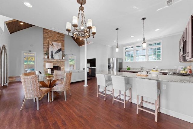 dining area with high vaulted ceiling, a stone fireplace, plenty of natural light, and dark wood-type flooring