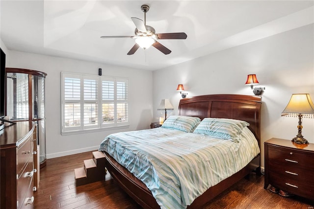 bedroom with a tray ceiling, ceiling fan, and dark wood-type flooring