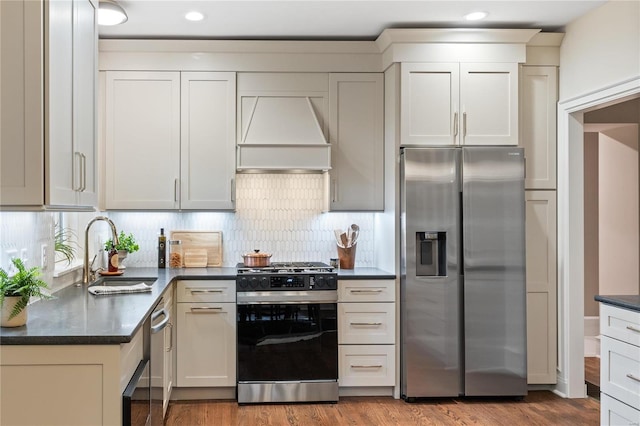 kitchen featuring custom exhaust hood, sink, tasteful backsplash, wood-type flooring, and stainless steel appliances