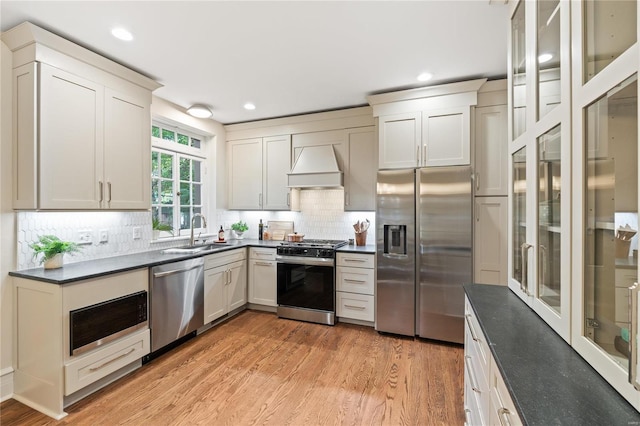 kitchen with light wood-type flooring, backsplash, custom range hood, stainless steel appliances, and sink