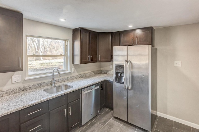 kitchen featuring sink, dark tile patterned floors, light stone countertops, dark brown cabinets, and stainless steel appliances