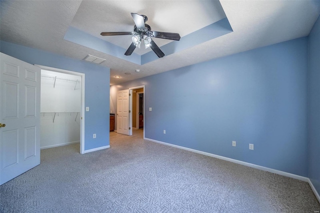 unfurnished bedroom with a closet, a textured ceiling, a raised ceiling, and ceiling fan