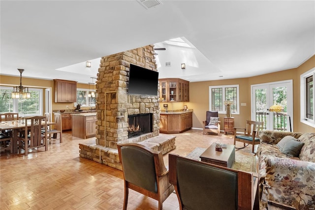 living room featuring a wealth of natural light, a notable chandelier, a stone fireplace, and light parquet floors