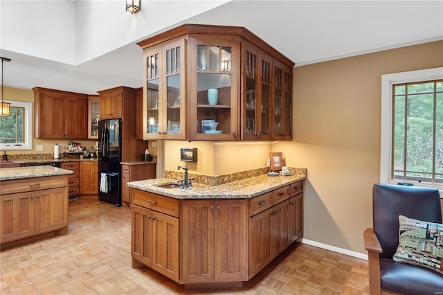 kitchen featuring black refrigerator, sink, light stone countertops, pendant lighting, and light parquet floors