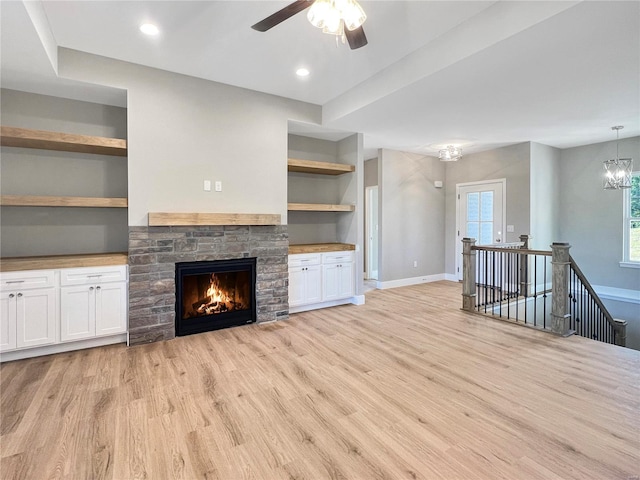 unfurnished living room featuring light hardwood / wood-style floors, ceiling fan with notable chandelier, a fireplace, and built in shelves