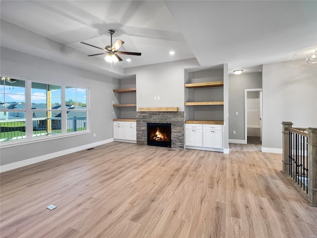 unfurnished living room featuring built in features, light hardwood / wood-style flooring, a fireplace, and ceiling fan