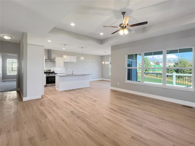 interior space with an island with sink, wall chimney exhaust hood, decorative light fixtures, stainless steel range, and white cabinets