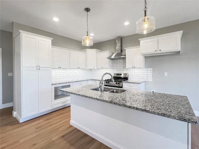 kitchen featuring sink, light wood-type flooring, hanging light fixtures, wall chimney exhaust hood, and white cabinets