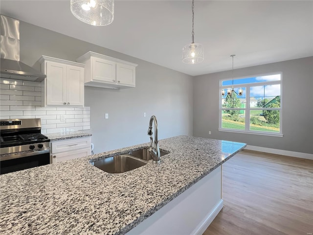 kitchen with wall chimney range hood, stainless steel gas stove, pendant lighting, white cabinets, and light stone counters