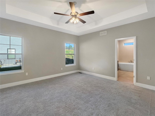 unfurnished bedroom with ensuite bathroom, light carpet, a tray ceiling, and ceiling fan