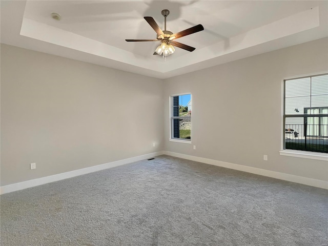 carpeted spare room with ceiling fan, a healthy amount of sunlight, and a tray ceiling