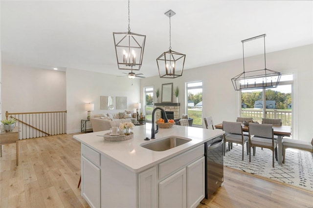 kitchen with dishwasher, sink, hanging light fixtures, light hardwood / wood-style flooring, and a kitchen island with sink