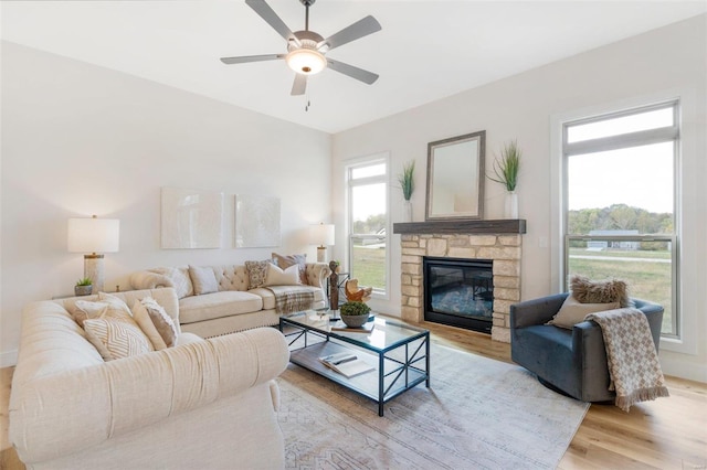 living room featuring a stone fireplace, light hardwood / wood-style floors, and ceiling fan