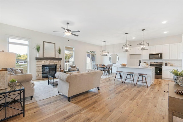 living room with a fireplace, sink, light wood-type flooring, and ceiling fan