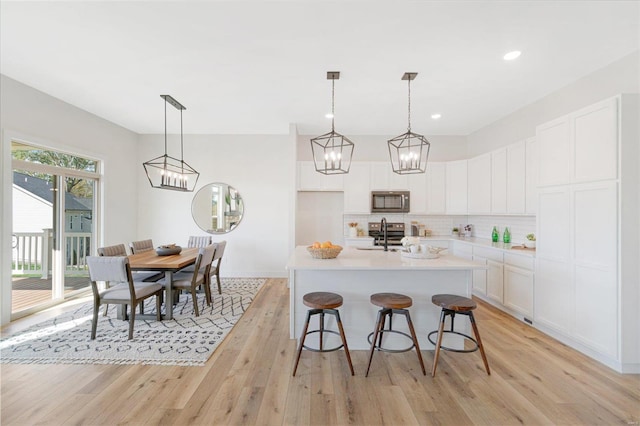 kitchen featuring light hardwood / wood-style flooring, decorative light fixtures, a kitchen island with sink, and white cabinets