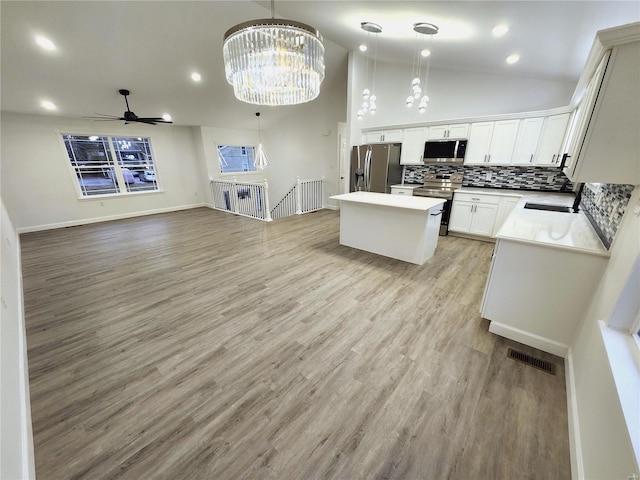 kitchen featuring hanging light fixtures, high vaulted ceiling, white cabinetry, ceiling fan with notable chandelier, and appliances with stainless steel finishes