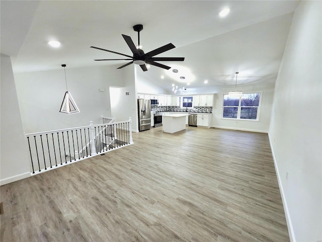 unfurnished living room featuring lofted ceiling, ceiling fan with notable chandelier, and light hardwood / wood-style floors