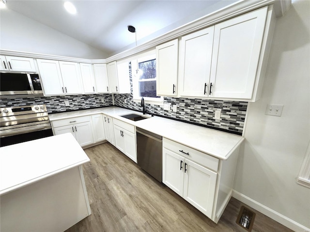 kitchen featuring decorative light fixtures, lofted ceiling, white cabinetry, appliances with stainless steel finishes, and sink