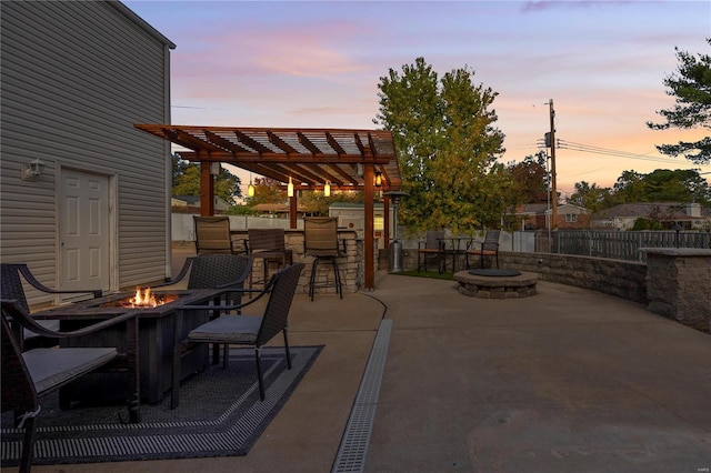 patio terrace at dusk featuring a pergola, a fire pit, and exterior bar