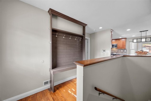 interior space featuring decorative backsplash, light hardwood / wood-style floors, pendant lighting, and kitchen peninsula