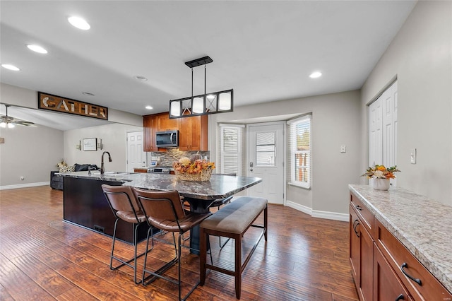 kitchen with decorative light fixtures, dark wood-type flooring, ceiling fan, a kitchen breakfast bar, and light stone counters