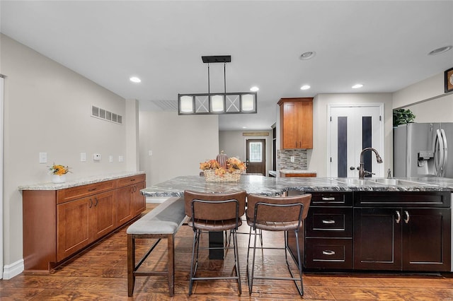 kitchen featuring dark hardwood / wood-style floors, pendant lighting, decorative backsplash, a kitchen island with sink, and stainless steel fridge