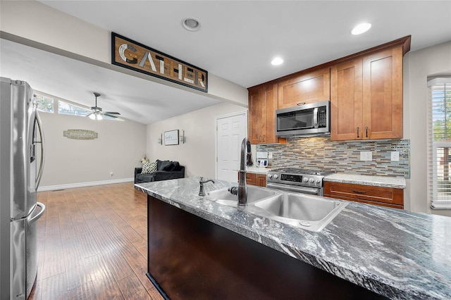 kitchen with ceiling fan, decorative backsplash, hardwood / wood-style flooring, appliances with stainless steel finishes, and light stone counters