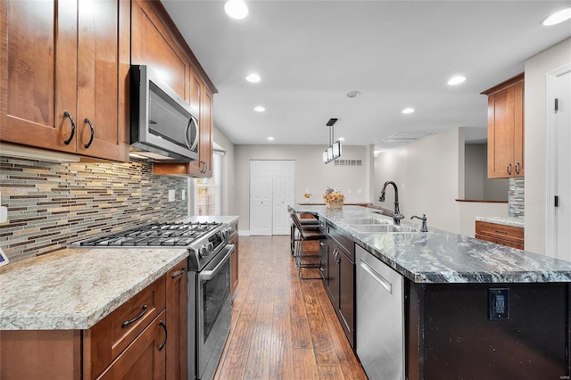 kitchen featuring a kitchen island with sink, sink, light stone counters, and stainless steel appliances