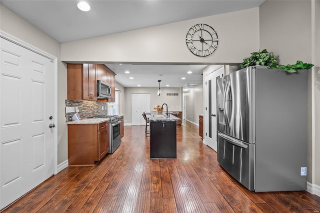 kitchen with appliances with stainless steel finishes, dark hardwood / wood-style floors, backsplash, a kitchen island with sink, and a kitchen breakfast bar