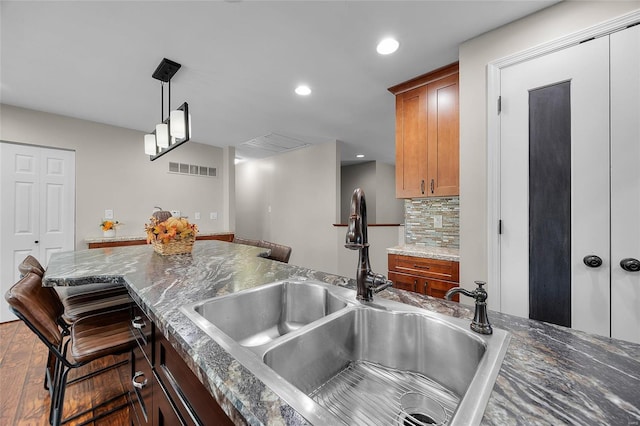 kitchen featuring decorative light fixtures, backsplash, dark stone countertops, a breakfast bar, and sink