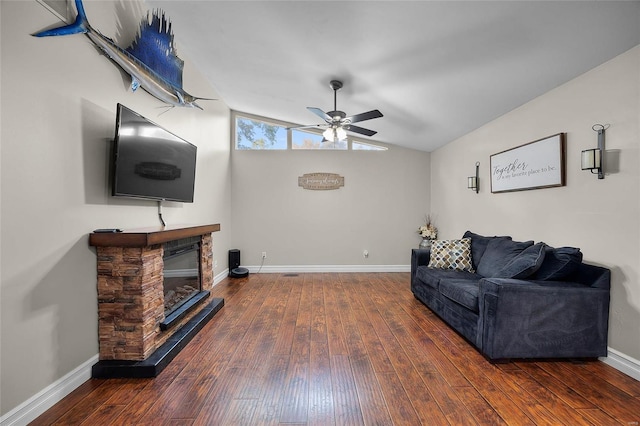 living room with ceiling fan, dark hardwood / wood-style flooring, a stone fireplace, and vaulted ceiling