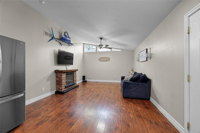 living room featuring ceiling fan, dark hardwood / wood-style floors, a stone fireplace, and vaulted ceiling