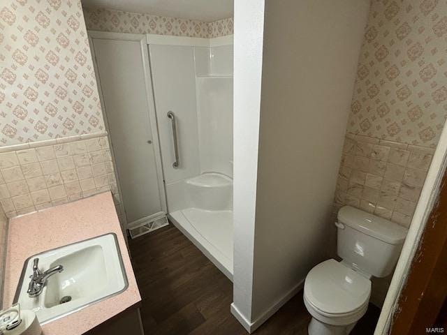 bathroom featuring wood-type flooring, toilet, walk in shower, tile walls, and vanity