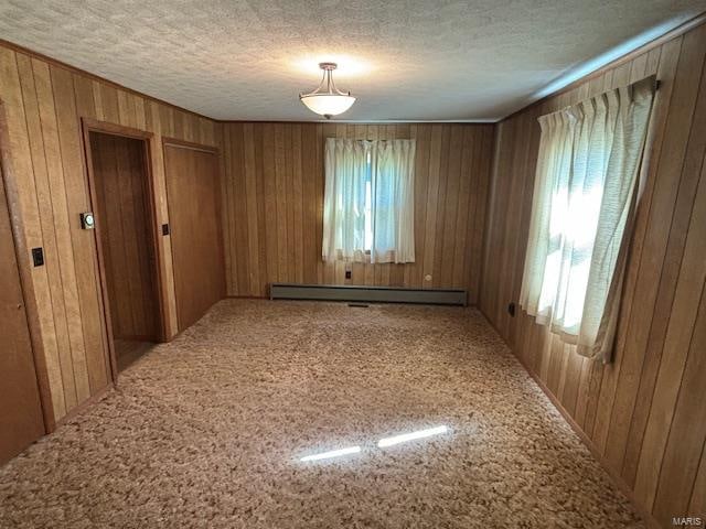 empty room with a baseboard radiator, a textured ceiling, and wood walls