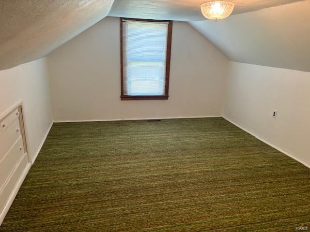 additional living space featuring vaulted ceiling, dark colored carpet, and a textured ceiling