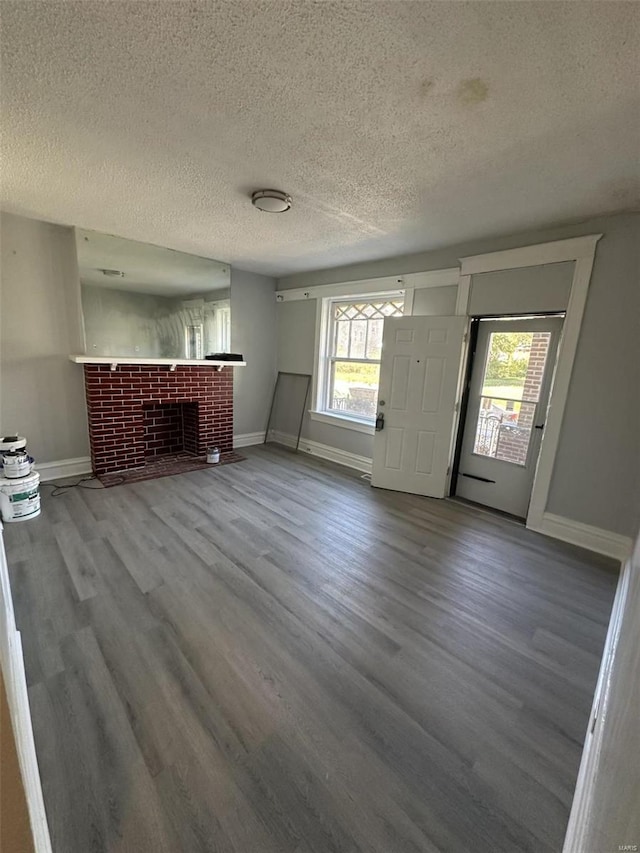 unfurnished living room featuring a textured ceiling, wood-type flooring, and a brick fireplace