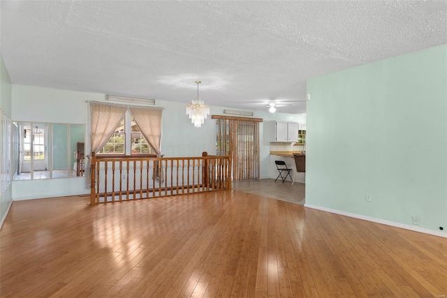 empty room featuring a textured ceiling, ceiling fan with notable chandelier, and light wood-type flooring