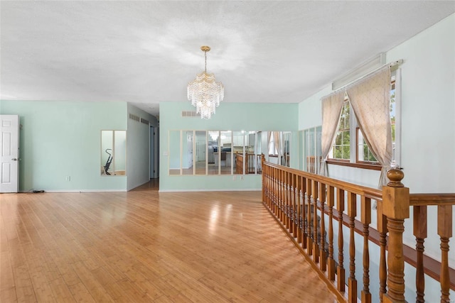 hallway with light hardwood / wood-style floors, a notable chandelier, and a textured ceiling