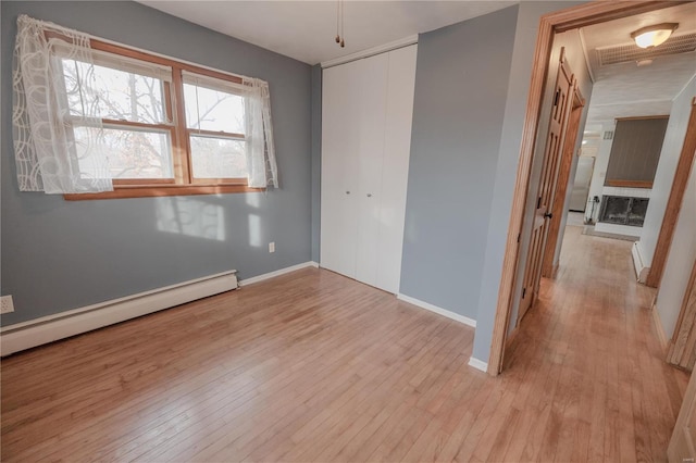 unfurnished bedroom with light hardwood / wood-style floors, a baseboard heating unit, and a closet