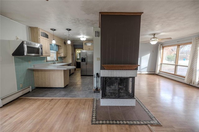 kitchen with ceiling fan, hanging light fixtures, a baseboard heating unit, kitchen peninsula, and appliances with stainless steel finishes