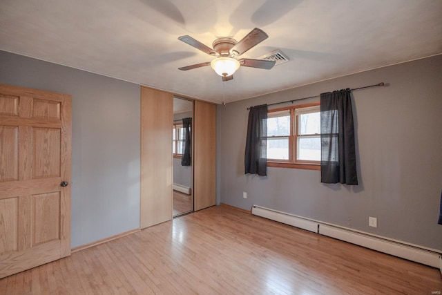 unfurnished bedroom with ceiling fan, light wood-type flooring, baseboard heating, and a closet