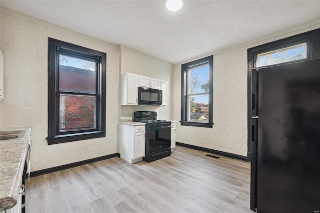 kitchen with white cabinetry, black appliances, and light hardwood / wood-style flooring