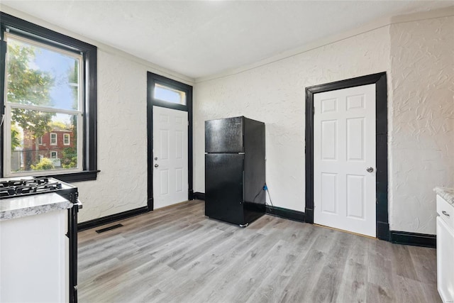 kitchen with gas range gas stove, white cabinetry, light hardwood / wood-style floors, and black fridge