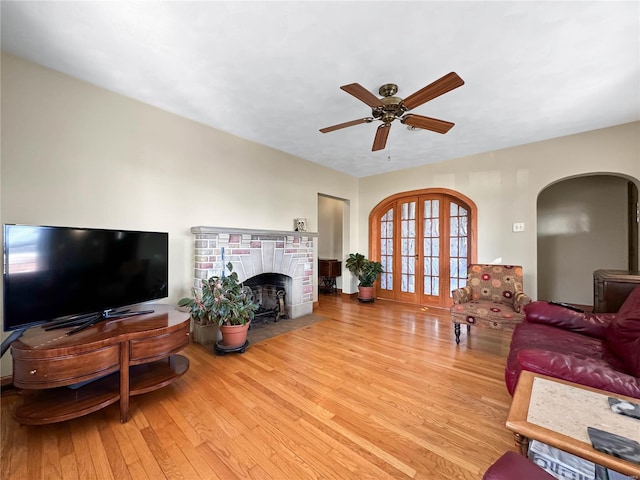 living room with a brick fireplace, light hardwood / wood-style floors, and ceiling fan