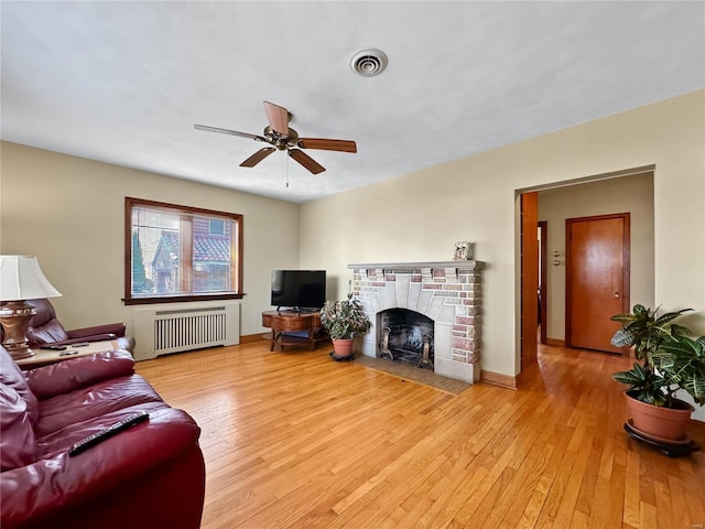 living room featuring ceiling fan, radiator heating unit, light wood-type flooring, and a brick fireplace